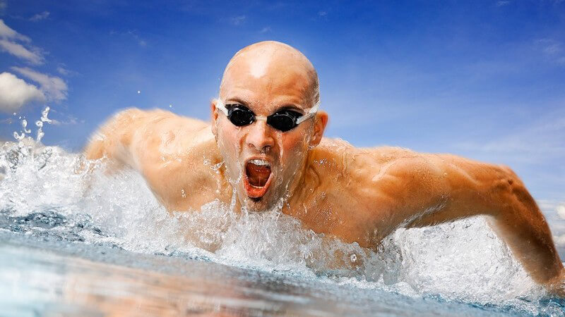 Muskulöser Mann mit Taucherbrille beim Schwimmen unter blauem Himmel