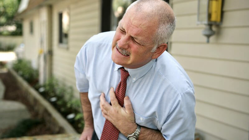 Älterer Mann nach vorn gekrümmt, hält sich Brust vor Schmerzen Herzinfarkt Herzattacke