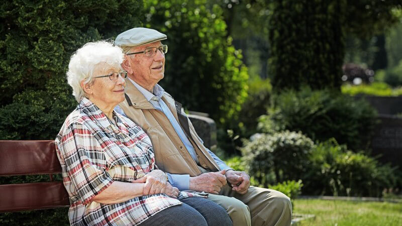 Senioren, älteres Paar sitzt auf Parkbank oder auf dem Friedhof