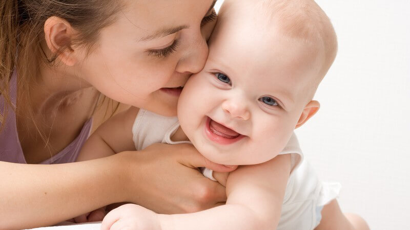 Junge Mutter küsst ihr lachendes Baby auf die Wange
