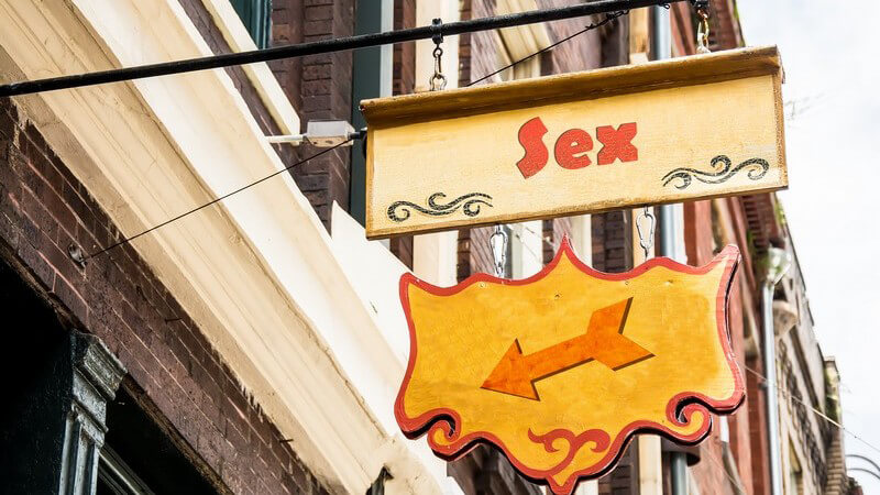 Altes Schild über einem Hauseingang mit der Aufschrift "Sex", darunter ein Pfeil, der zum Eingang zeigt