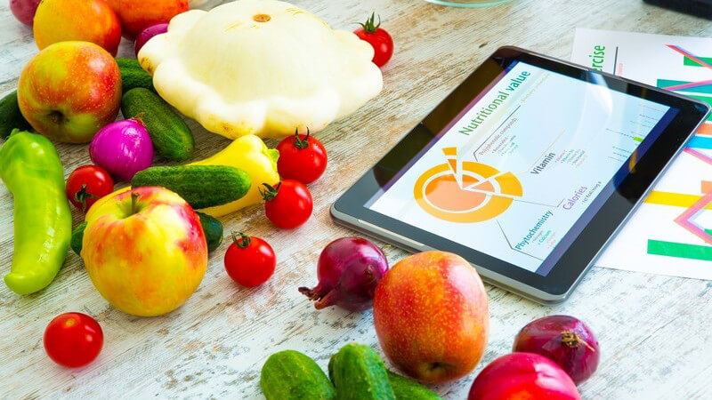Tablett-PC mit Ernährungs-App auf einem Tisch mit einer bunten Mischung an gesunden Obst- und Gemüsesorten