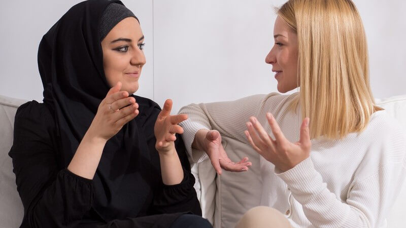 Zwei junge Frauen unterschiedlicher Ethnie im Gespräch, Muslimin mit Kopftuch und blonde Christin