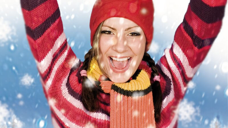 Junge Frau mit Zöpfen in geringelter, bunter Schneebekleidung o Winterbekleidung mit Mütze und Schal im Schnee, fröhlich
