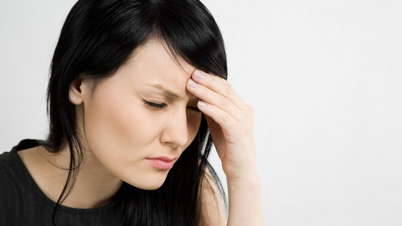 Dunkelhaarige Frau fasst sich an die Stirn, hat Kopfschmerzen