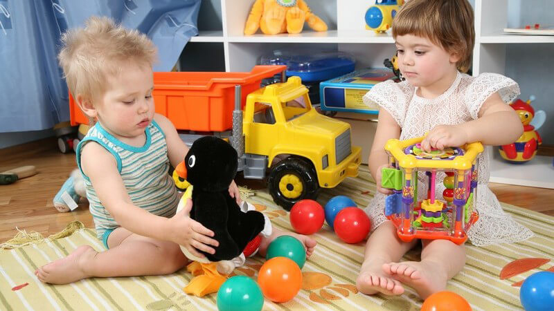 Zwei Kleinkinder mit Spielzeug im Spielzimmer