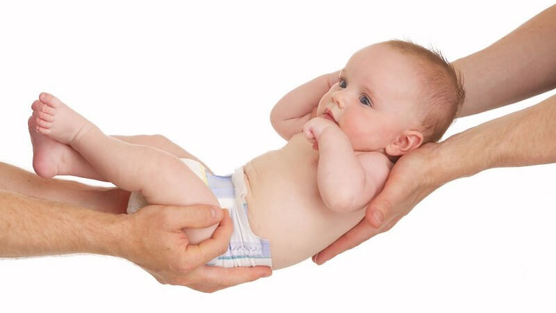 Baby in Windeln wird von zwei Händen vorne und hinten gehalten und geschaukelt