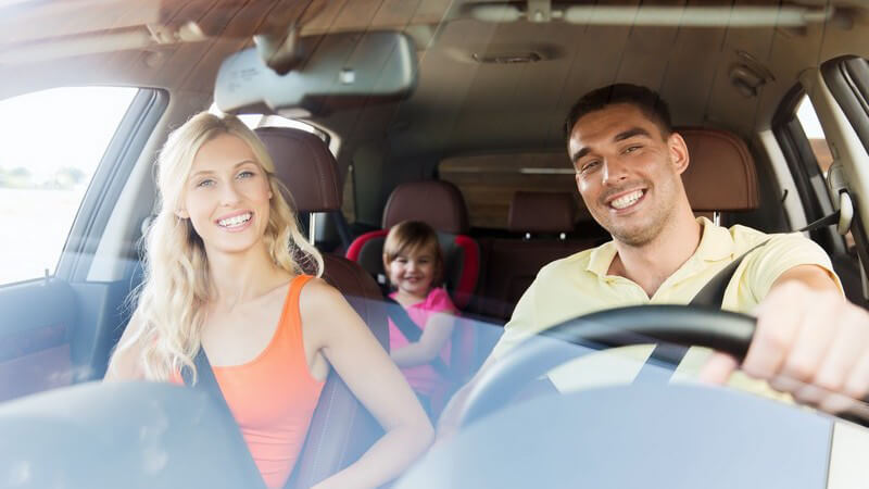 Junge Familie fährt lächelnd mit dem Auto, kleines Mädchen im Kindersitz