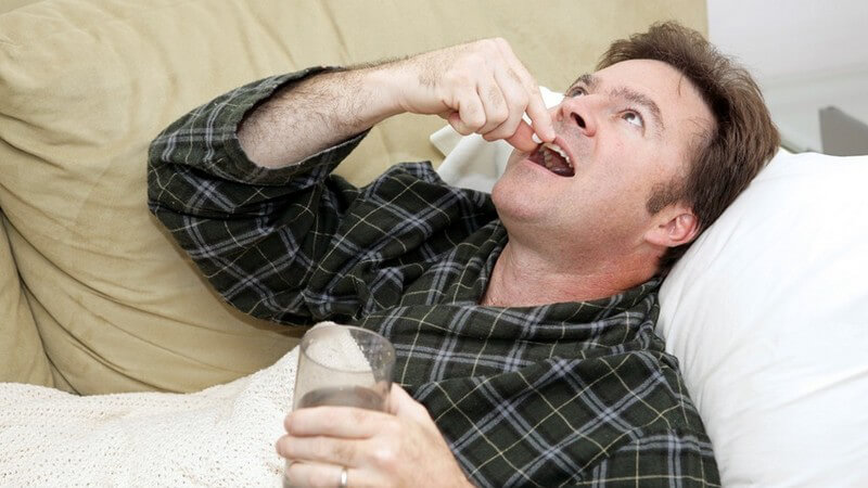 Krank - Mann liegt auf der Couch und nimmt eine Tablette