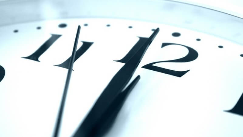 Nahaufnahme weiße Uhr mit schwarzem Ziffernblatt zeigt vier Sekunden vor Zwölf