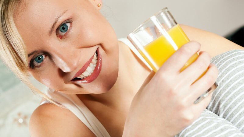 Frau mit Glas Orangensaft lacht in Kamera