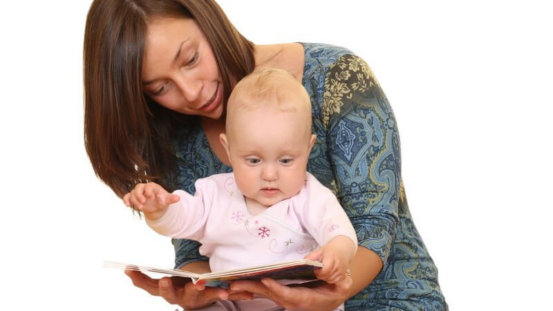 Junge Mutter hat Baby auf Schoß, schauen gemeinsam Bilderbuch an