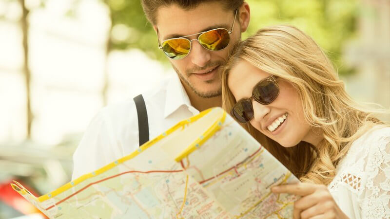 Junges Paar mit Sonnenbrillen sieht sich Stadtplan an, Städtetrip im Sommer