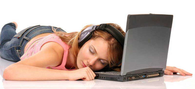 Junge Frau liegt auf Bauch vor ihrem Notebook und hört über Kopfhörer Musik