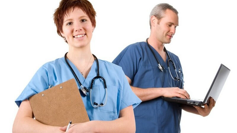 Junge Frau mit blauem Arzt-Hemd, Krankenakte und Stetoskop vorne, hinten grauhaariger Arzt, Stetoskop, mit Laptop