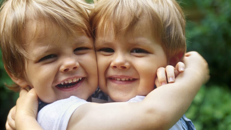 Zwillinge - zwei kleine Jungs halten sich Wange an Wange im Arm