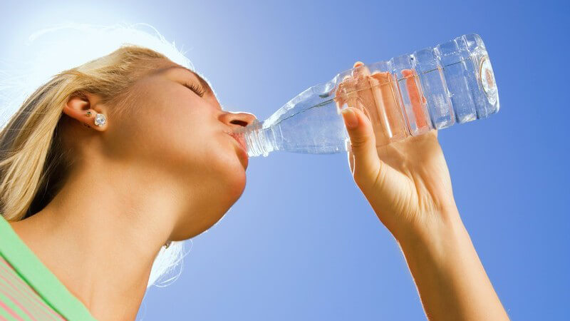 Ansicht von unten: Junge Frau trinkt Wasser aus Plastikflasche unter blauem Himmel
