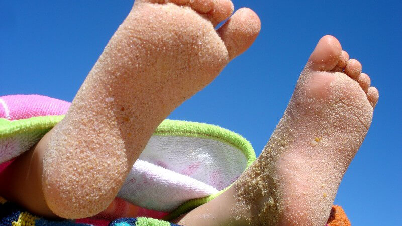 Kinderfüße auf Strandtuch, Sand auf Fußsohlen, blauer Himmel