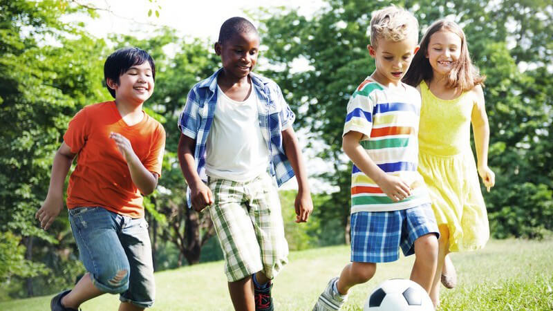 Drei Jungen und ein Mädchen spielen Fußball auf einer Wiese im Park