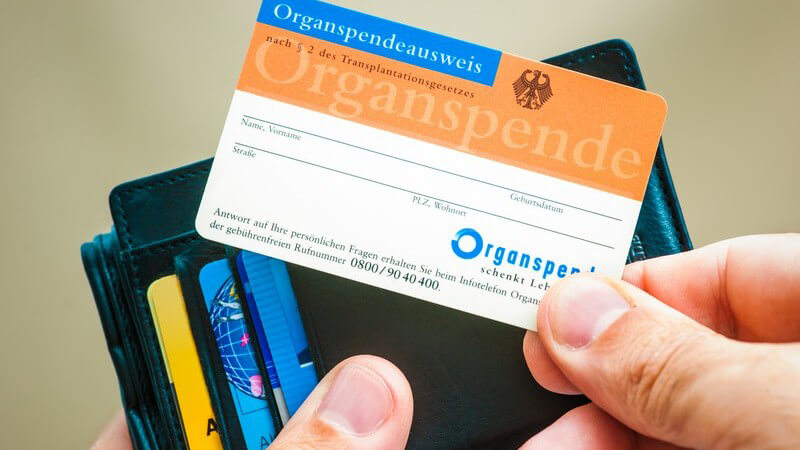 Hand hält einen Organspendeausweis vor einem schwarzen Portemonnaie