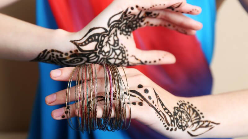 Frau mit Henna-Tattoos auf beiden Händen, die Finger stecken in Armbändern