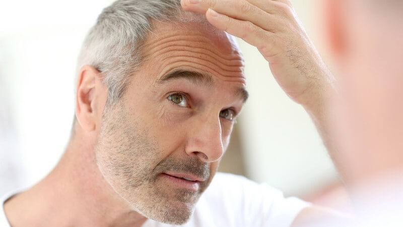 Haarausfall - älterer Mann schaut seine grauen Haare im Spiegel an
