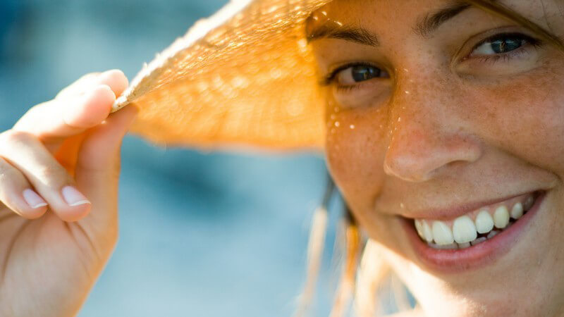 Gesicht einer jungen Frau mit Sonnenhut, lächelt in Kamera