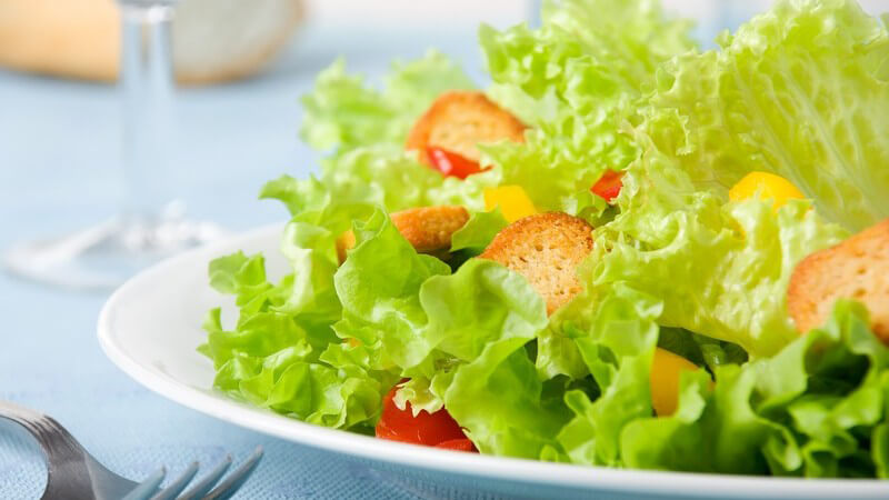 Grüner Salat mit Crutons, daneben eine Gabel, dahinter Brot und ein Glasstiel