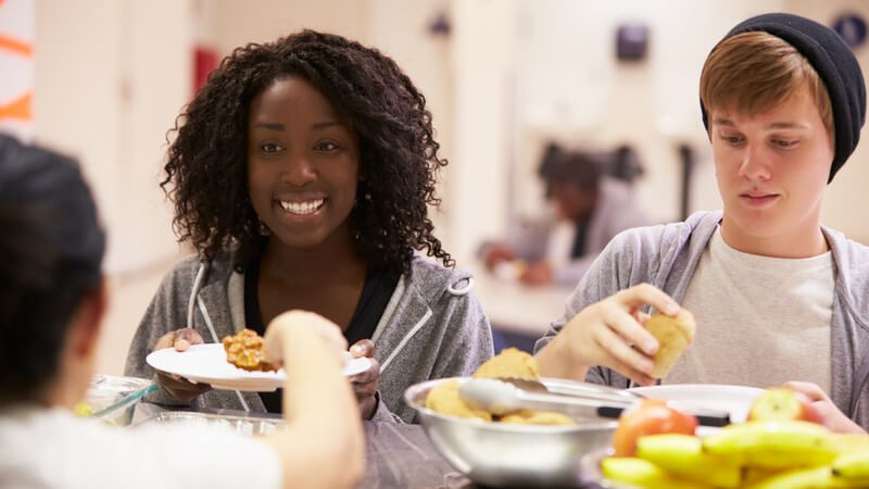 Essensausgabe in einer Großküche an zwei Teenager, dunkel- und hellhäutig