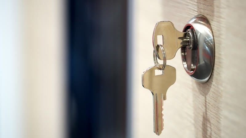 Schlüssel mit anhängendem Ersatzschlüssel steckt im Schlüsselloch einer Tür