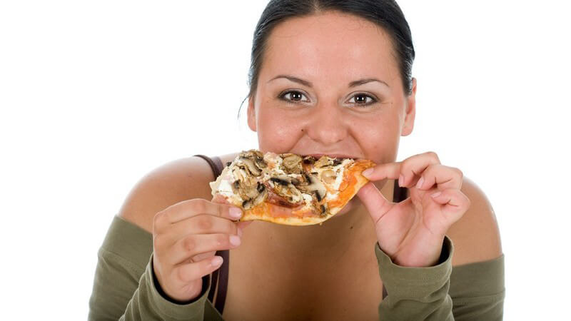 Dunkelhaarige junge Frau beißt mit Appetit in ein Stück Pizza mit Pilzen vor weißem Hintergrund