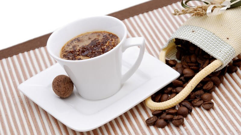 Frisch aufgebrühter Kaffee in Tasse umgeben von Kaffeebohnen auf Set