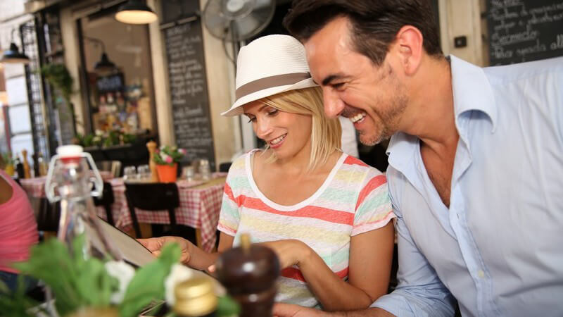 Paar im Sommerurlaub sitzt im Restaurant und schaut Speisekarte durch