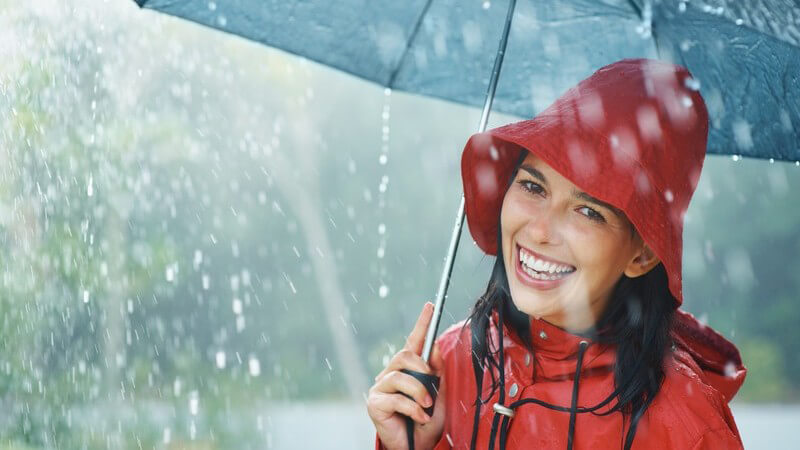 Junge Frau mit Regenhut und -jacke unter Regenschirm