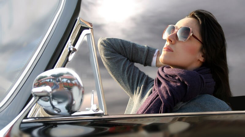 Frau sitzt im eleganten Cabrio mit Schal und Sonnenbrille