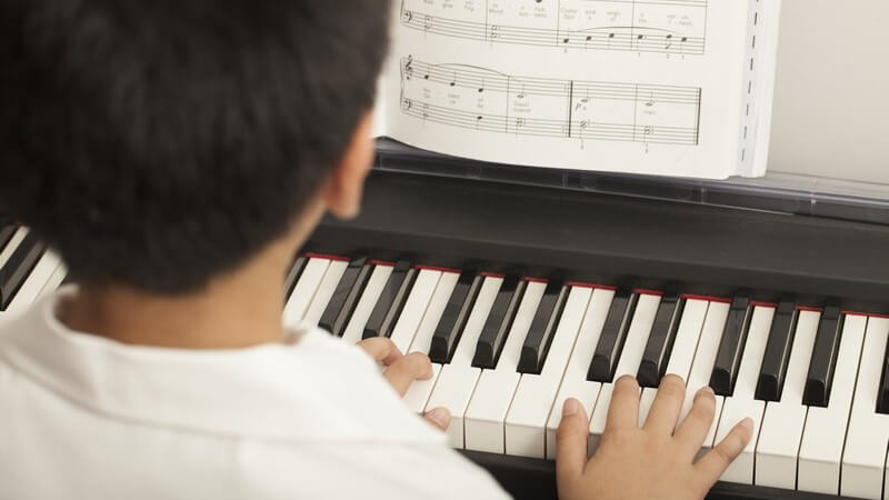 Asiatischer Junge spielt Klavier nach Noten