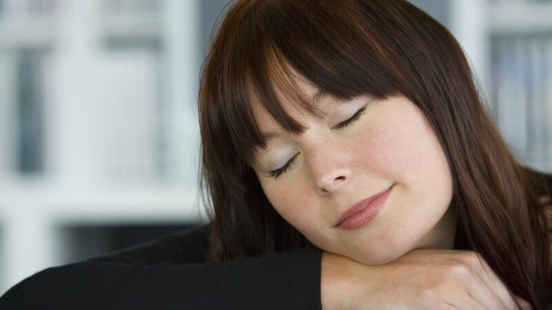 Dunkelhaarige Frau mit geschlossenen Augen lehnt ihren Kopf entspannt auf den Arm