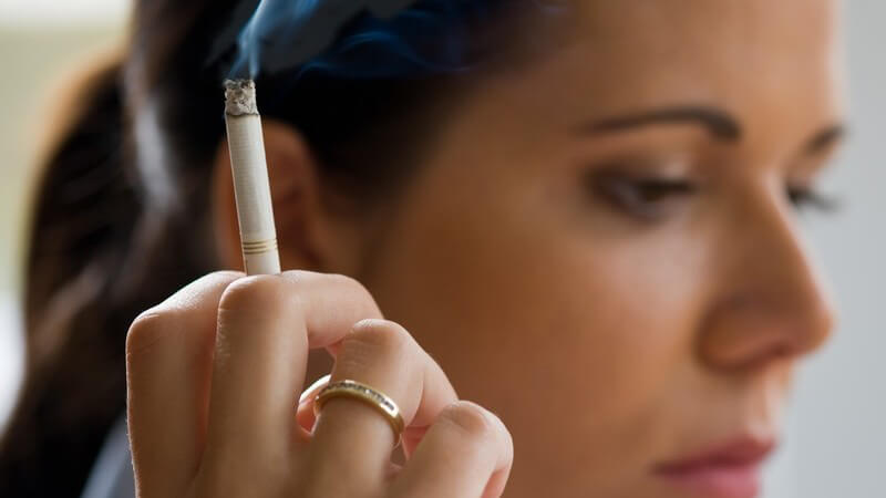 Seitenansicht junge dunkelhaarige Frau hält qualmende Zigarette in Hand