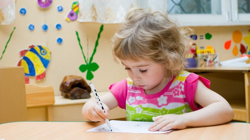 Kleines Mädchen sitzt am Tisch und malt mit Filzstiften