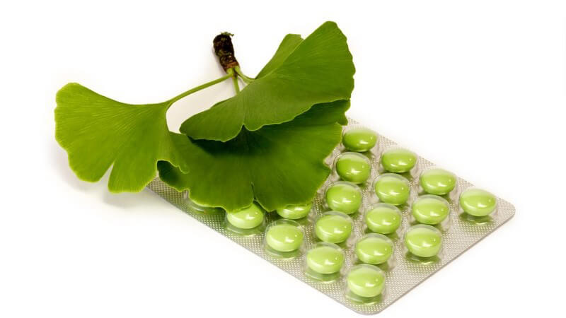 Palette mit grünen Tabletten, darauf Ginkoblätter, weißer Hintergrund