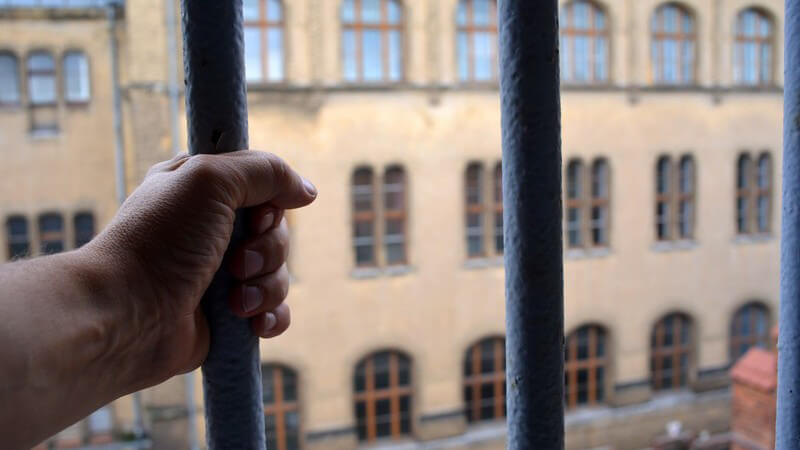 Hand am Gitterstab eines Gefängnisfensters