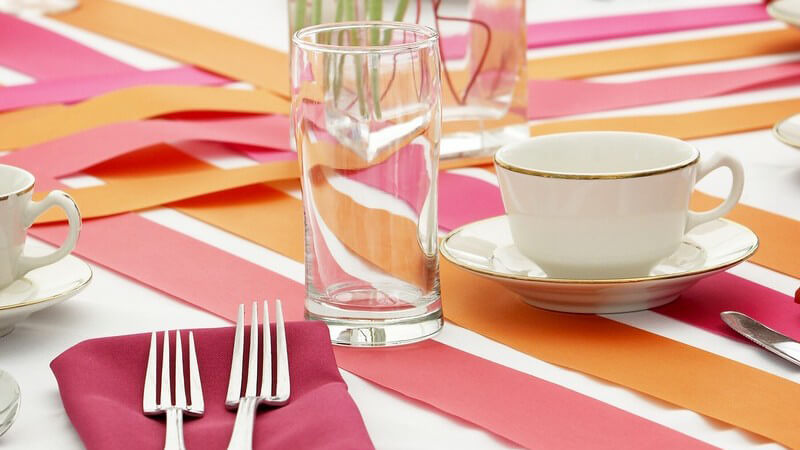 Gedeckter Tisch mit rosanen und orangen Farben, pinke Blumen in Vase