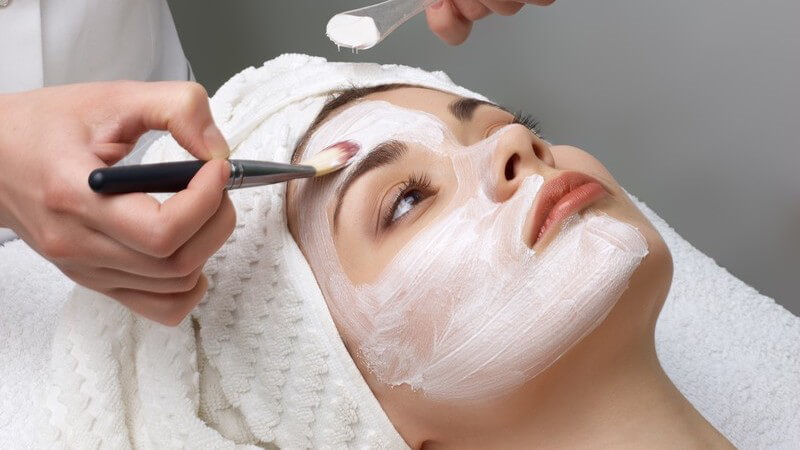 Junge Frau im Kosmetiksalon bekommt Gesichtsmaske mit Pinsel aufgetragen