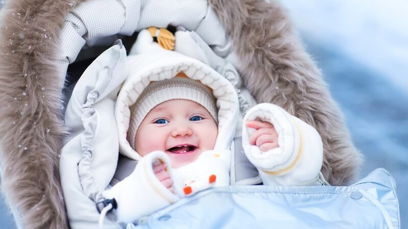 Lächelndes Baby im Kinderwagen im Winter, dick eingepackt