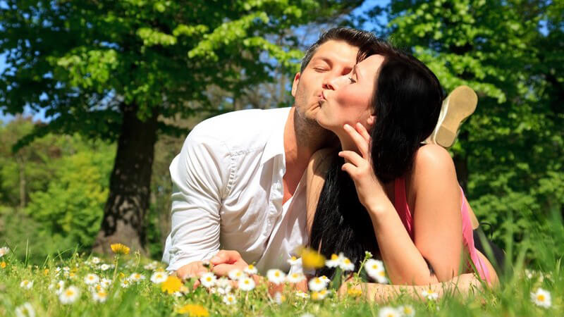 Junges Paar liegt auf Wiese im Park, küsst sich