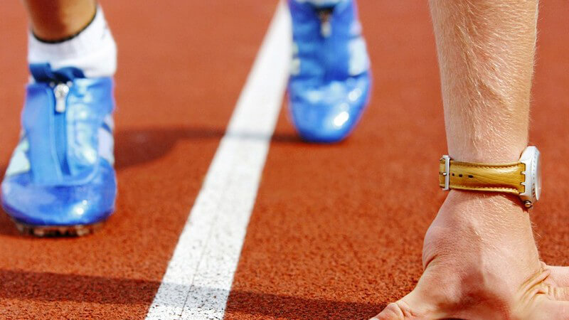 Sprinter mit blauen Laufschuhen und goldener Uhr in Startposition