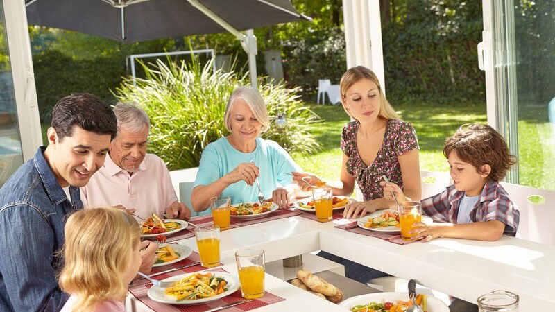 Drei Generationen einer Familie sitzen gemeinsam am Tisch im Wintergarten und essen