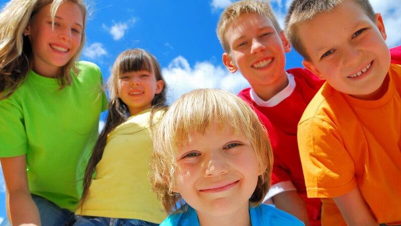 Gruppe von fünf Kindern lächelt in Kamera unter blauem Himmel