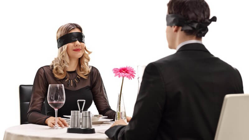 Mann und Frau haben ein Blind Date, sitzen sich mit verbundenen Augen gegenüber