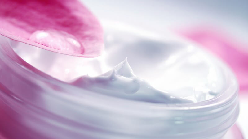 Nahaufnahme Tiegel Dose mit weißer Gesichtscreme oder Feuchtigkeitscreme, pinkes Blütenblatt am Rand mit Creme
